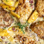 Golden-brown chicken breasts in a creamy sauce with peach slices, bacon bits, fresh thyme, and visible herbs, all garnished with sprigs of thyme—a delightful twist inspired by Chicken Normandy with Cider and Apples.