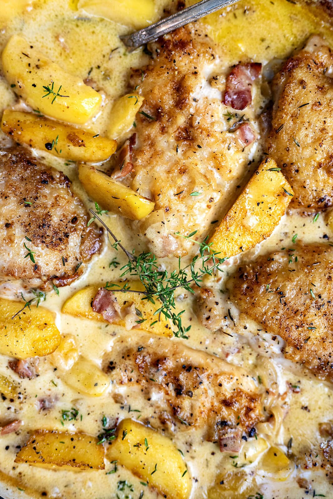 Golden-brown chicken breasts in a creamy sauce with peach slices, bacon bits, fresh thyme, and visible herbs, all garnished with sprigs of thyme—a delightful twist inspired by Chicken Normandy with Cider and Apples.