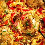 Golden-brown chicken thighs with orzo pasta, red bell pepper strips, browned Italian sausage, red drop peppers, parsley and fennel fronds, all mixed together in a skillet.