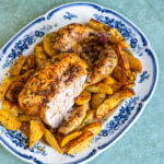 Greek roast chicken with crispy golden skin, partly carved, on a blue and white platter with lemon potatoes