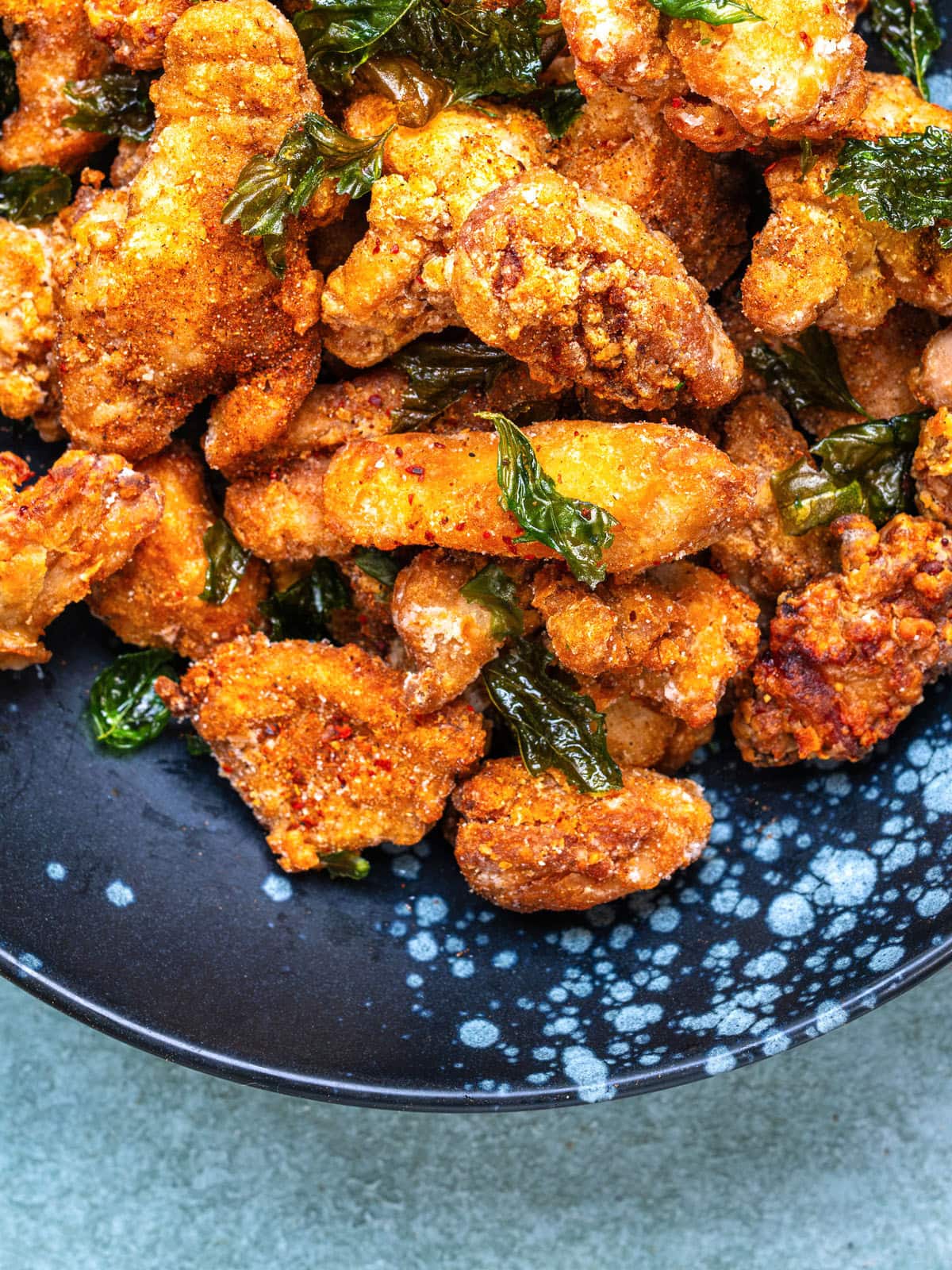 Crispy Taiwanese fried chicken pieces tossed with fried Thai basil on a dark blue speckled plate