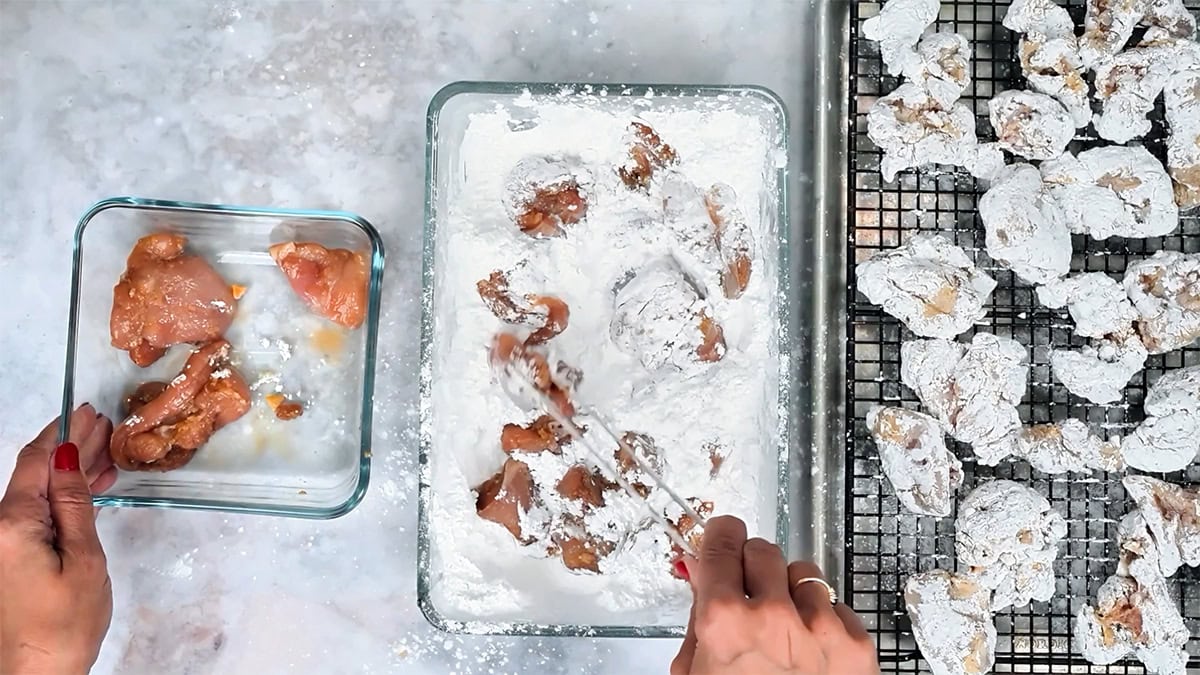 Coating marinated chicken pieces in coarse sweet potato starch, with dredged pieces resting on a rack