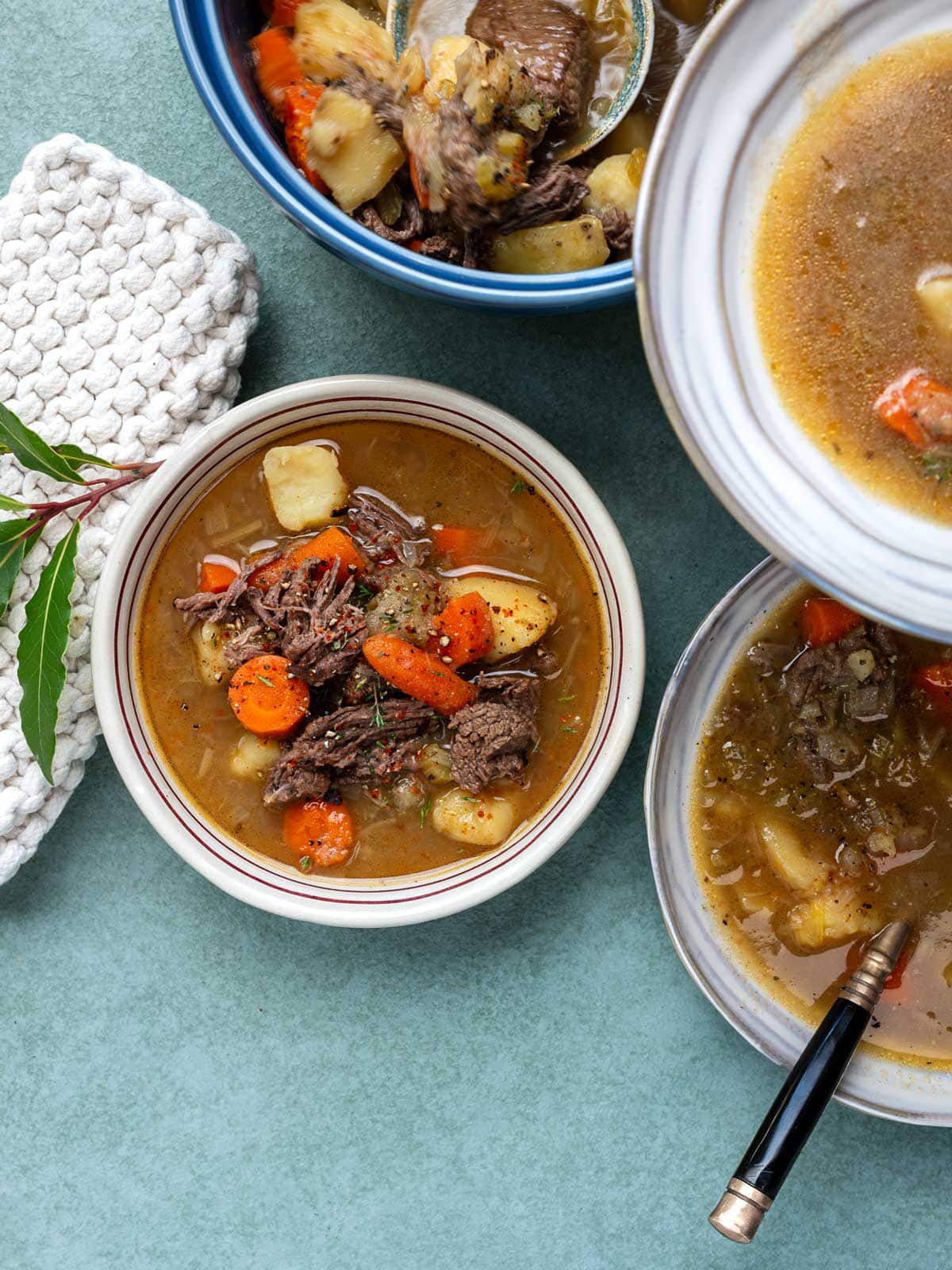 Three bowls of beef soup with potatoes and carrots on a teal surface.
