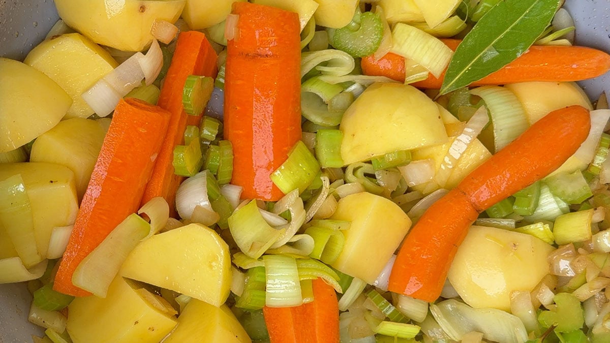 Potatoes, carrots, celery and sliced leek in a pot with a bay leaf for beef soup.