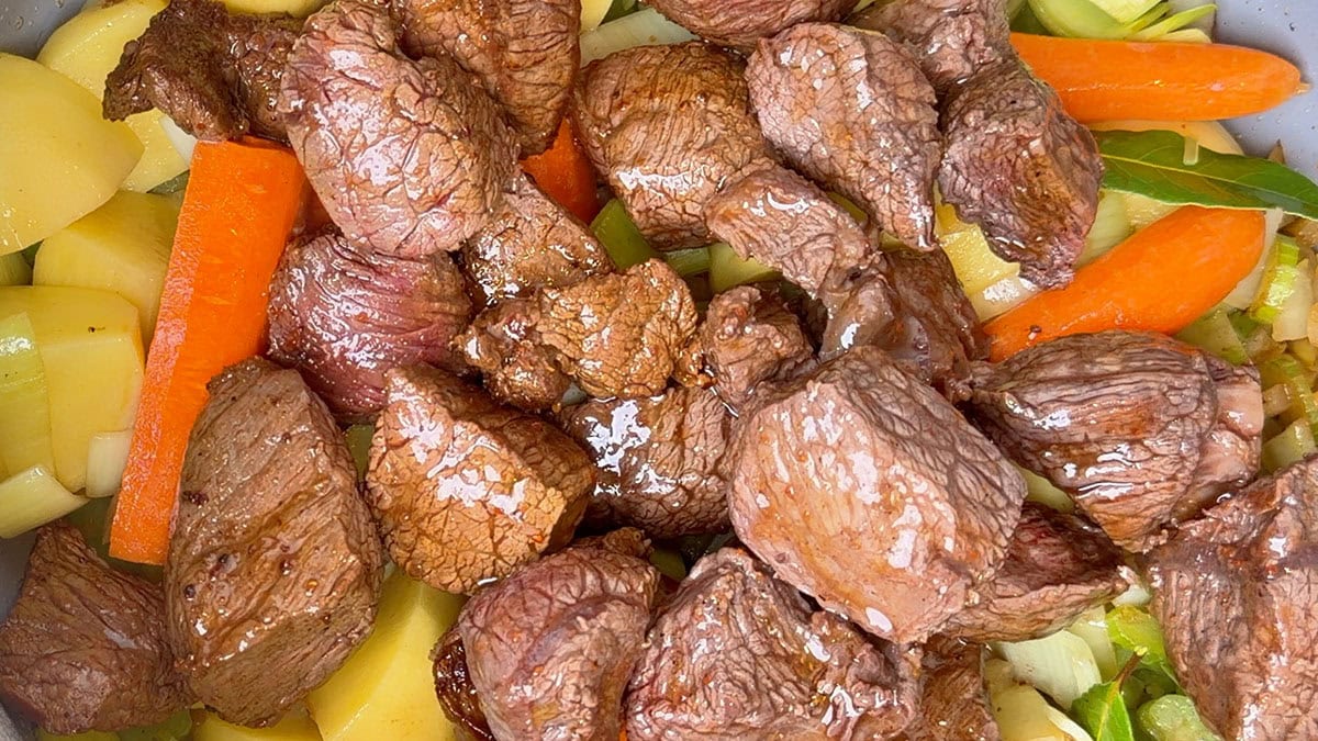 Seared beef returned to the pot with potatoes, carrots and celery before simmering.