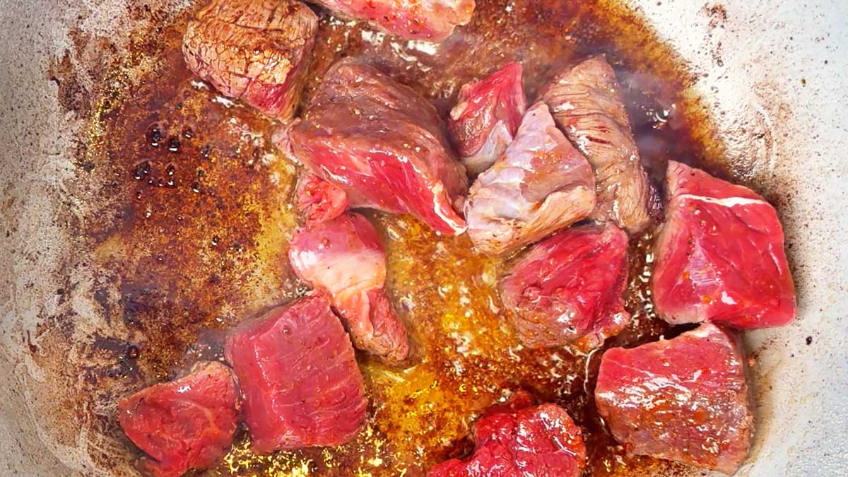 Cubes of seasoned beef searing in a hot pan for the soup.