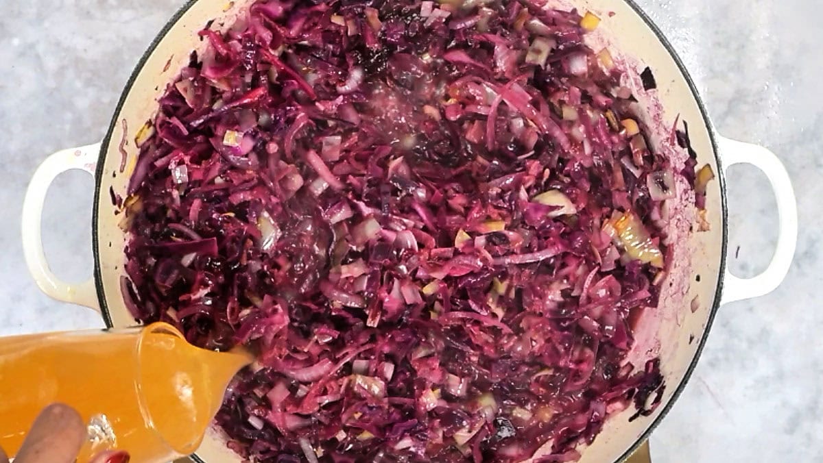 Beer being poured over shredded red cabbage and onions in a skillet