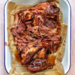 Braised ham hock with a sticky maple mustard glaze, pulled into tender pieces and served in a white enamel tray lined with paper.