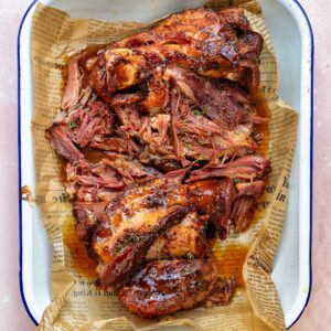 Braised ham hock with a sticky maple mustard glaze, pulled into tender pieces and served in a white enamel tray lined with paper.