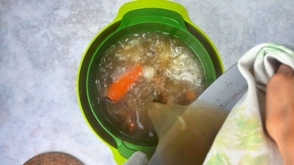 Straining the ham hock braising liquid and vegetables through a sieve into a bowl.