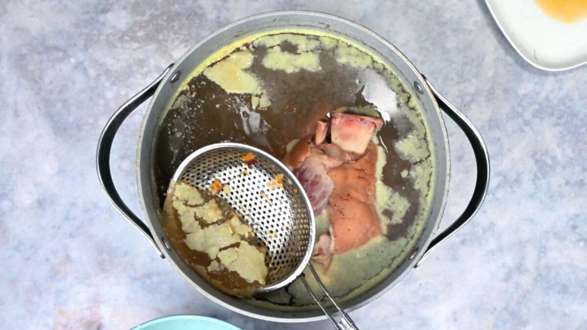Skimming the ham hock braising liquid with a small mesh strainer before storing it as stock.