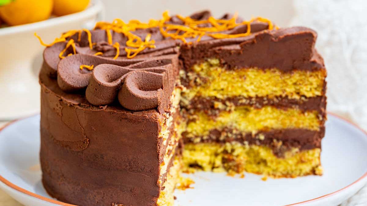 Chocolate orange layer cake with a slice cut away, showing three golden orange sponge layers filled with chocolate ganache.