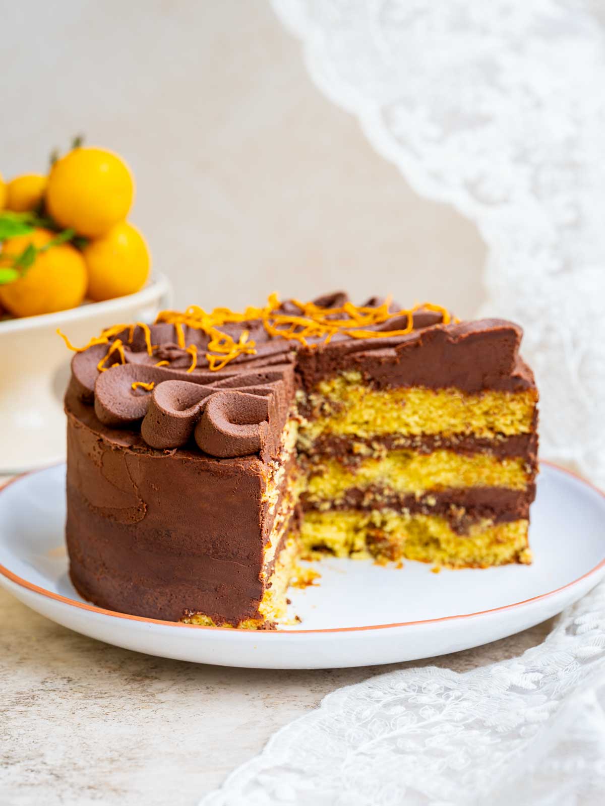 A layered chocolate orange cake with frosting, topped with orange zest, with one slice removed.