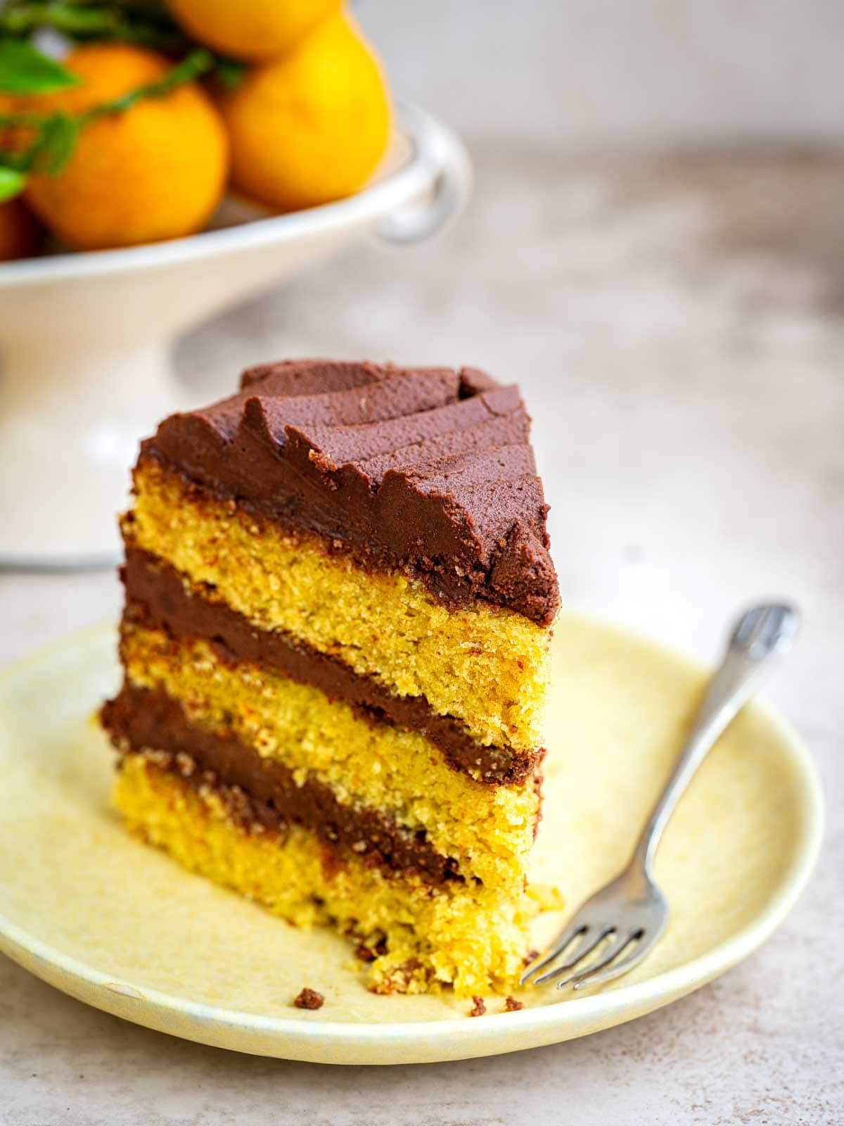 A slice of three-layer chocolate orange cake on a yellow plate with a fork.