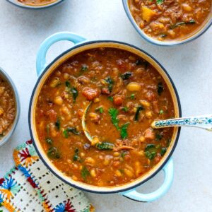 A large blue pot filled with ham and bean soup, surrounded by two smaller bowls of the same dish and a crocheted coaster.