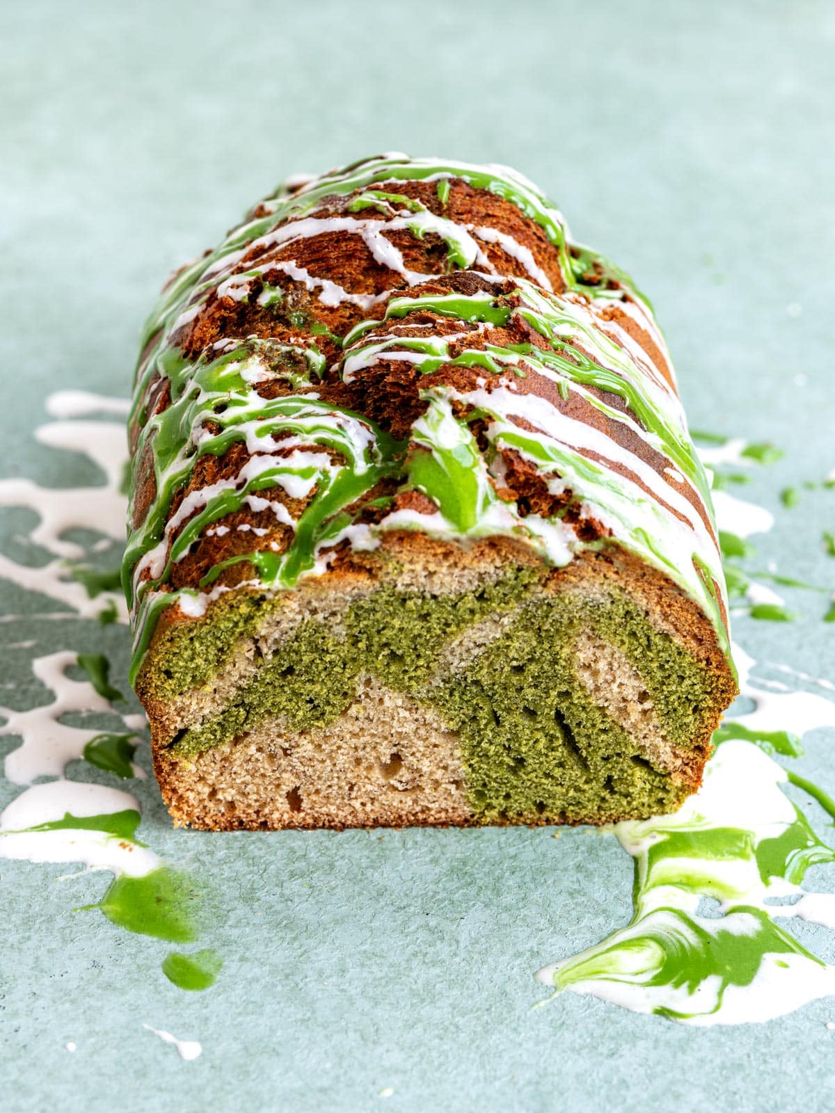 A loaf of marbled matcha banana bread drizzled with white and green icing.