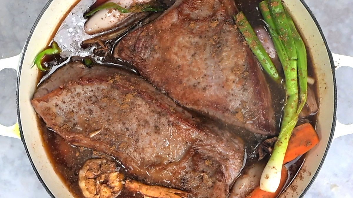 The two seared brisket halves back in the Dutch oven with the soy and broth braising liquid, garlic, green onions and carrots, ready to go into the oven.