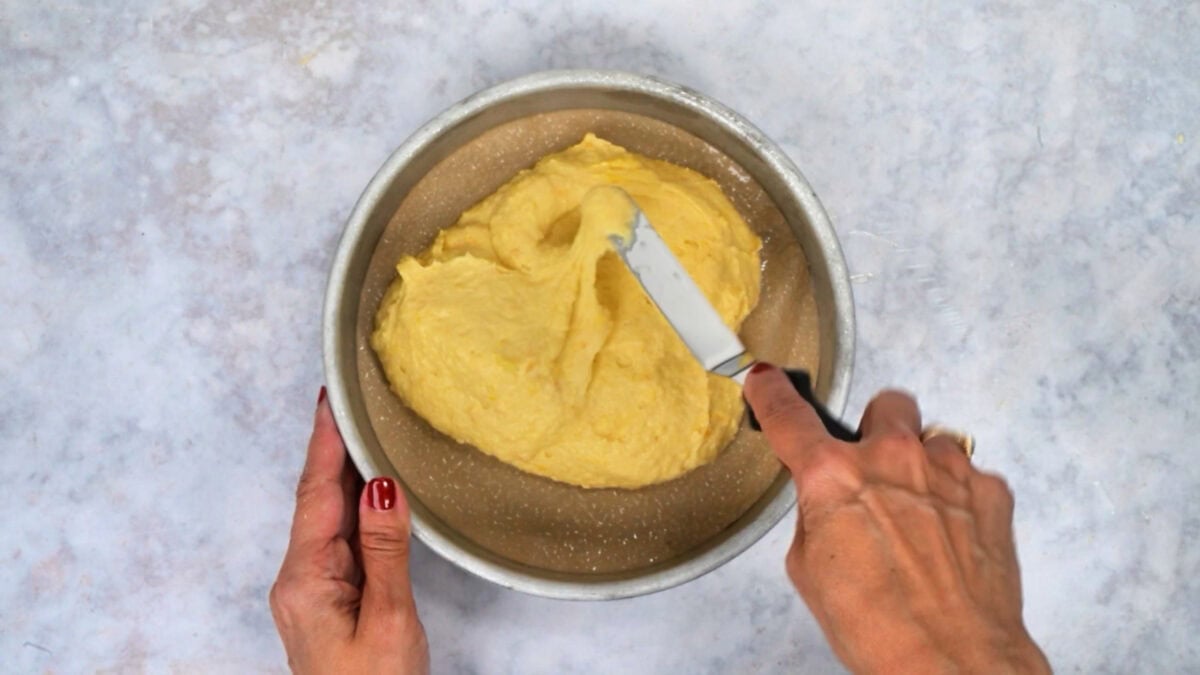 Spreading orange cake batter evenly in a round cake pan with an offset spatula.