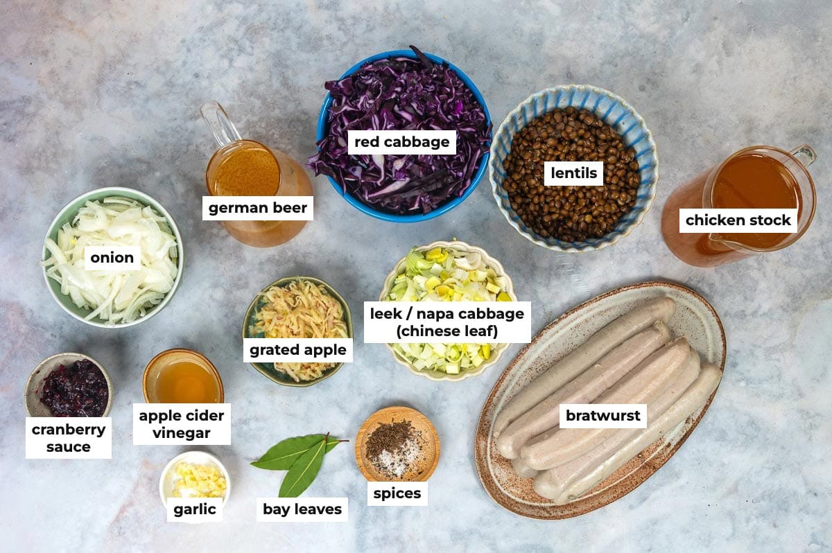 Labeled ingredients for bratwurst casserole: onion, German beer, red cabbage, lentils, chicken stock, cranberry sauce, apple cider vinegar, garlic, grated apple, leek and Napa cabbage, bay leaves, spices and bratwurst