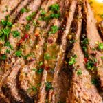 Close-up of sliced slow cooker brisket in miso onion gravy, garnished with chopped parsley and red pepper flakes